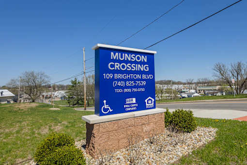 A blue sign for Munson Crossing is displayed in front of a grassy area.