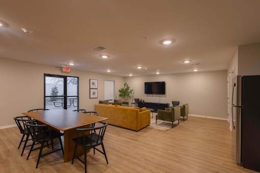 A room with a long table and chairs, a couch, a television, and a plant.
