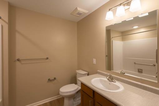 A bathroom with a toilet, sink, mirror, and a towel bar.