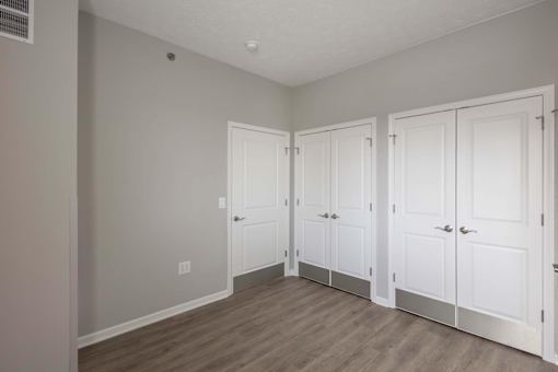 Three white doors are closed in a room with wood flooring.