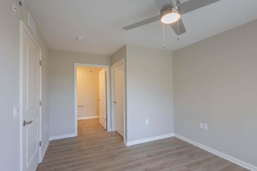 A room with a ceiling fan and light fixture, and a doorway leading to another room.