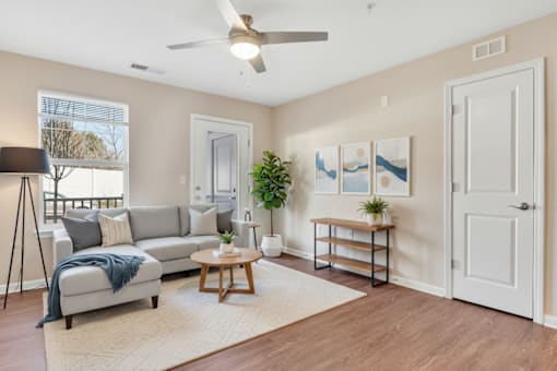 A living room with a grey sofa, a wooden coffee table, a white door, a white ceiling fan, and a white wall.