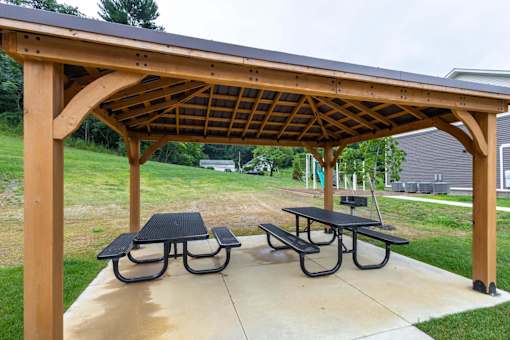 A wooden pergola with a black roof and two picnic tables.