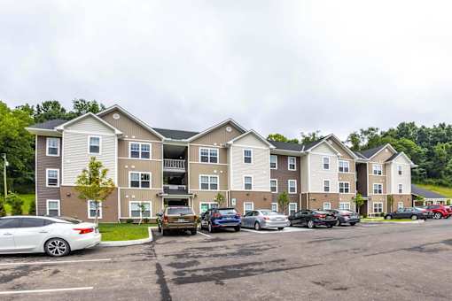 A parking lot in front of a two-story apartment building with cars parked in the lot.