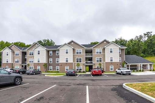 A parking lot in front of a large apartment building with cars parked.