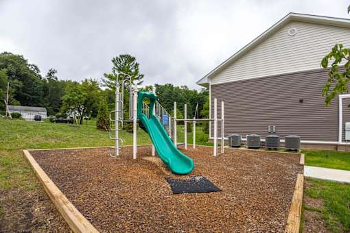 A playground with a green slide and a brown mulch area.
