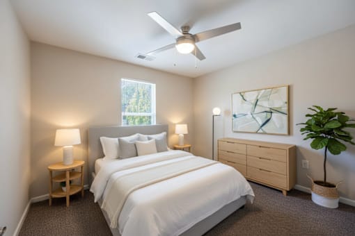 A bedroom with a large bed, a ceiling fan, and a window with a view of trees.