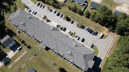 A large building with a grey roof is surrounded by a parking lot.