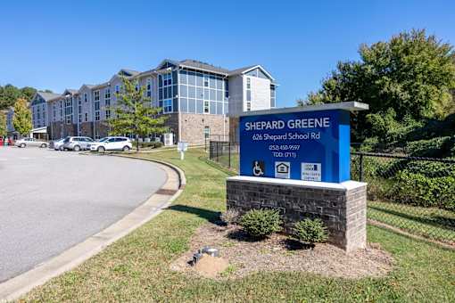 A sign for Shepard Greene stands in front of a parking lot.