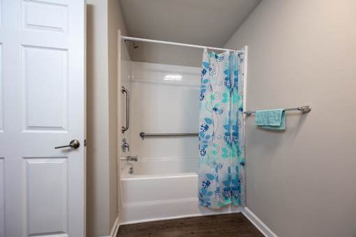 A white door is open to a bathroom with a white tub and a blue shower curtain.