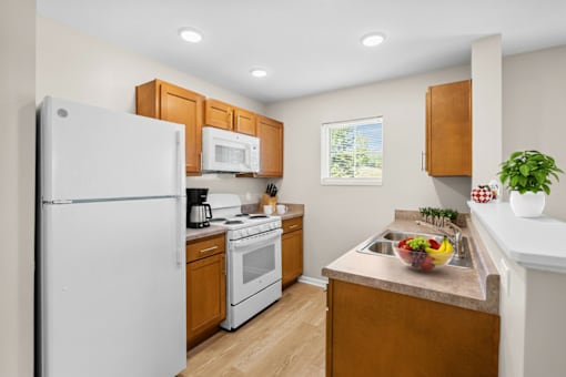 A kitchen with a white refrigerator, wooden cabinets, and a window.