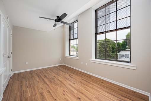 A room with a ceiling fan and a window overlooking a house.