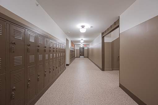 A long hallway with brown lockers on the left and a white door at the end.