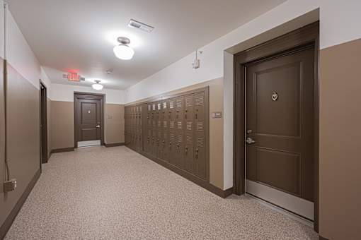 A long hallway with brown doors and a red exit sign.