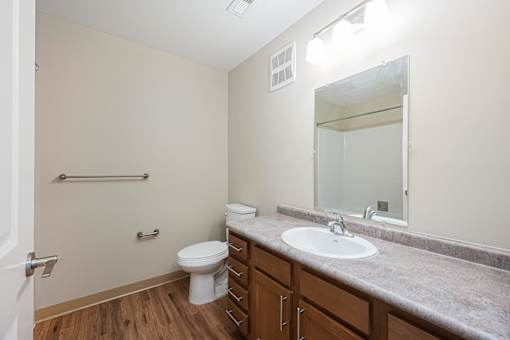 A bathroom with a toilet, sink, mirror, and a wooden floor.