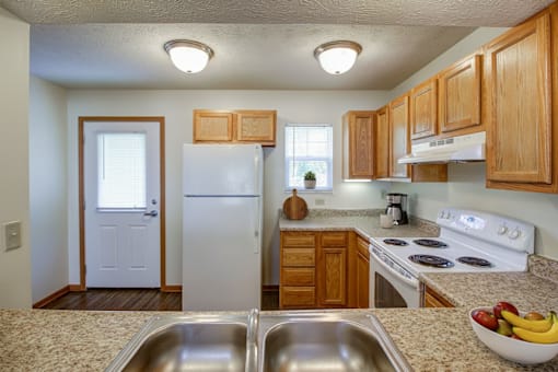 A kitchen with a white refrigerator, wooden cabinets, and a bowl of fruit on the counter.