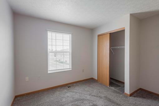 A room with a carpeted floor, a window with blinds, and a wooden door.