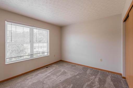 A room with a carpeted floor and a window with blinds.