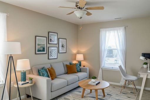 A living room with a beige couch, a wooden coffee table, and a ceiling fan.
