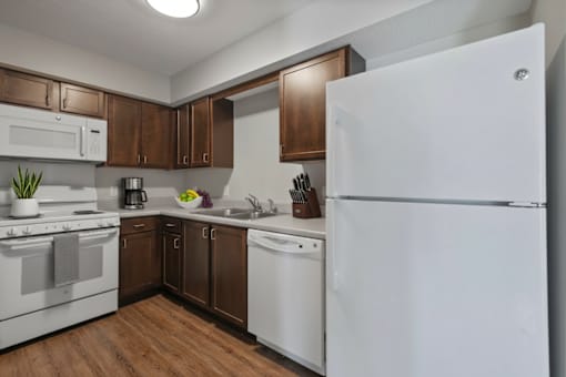 A white refrigerator stands in a kitchen with brown cabinets and white appliances.