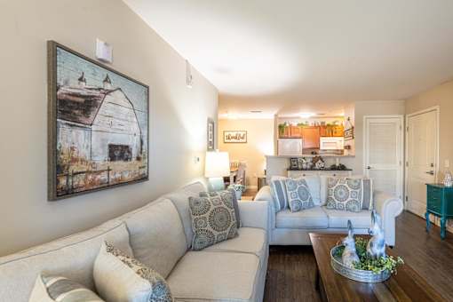 A living room with a grey couch and a painting of a barn on the wall.