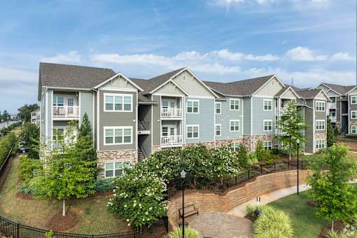 A large apartment complex with a black fence and a brick walkway.