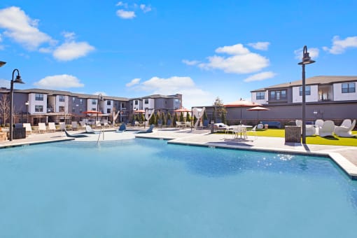 a resort style pool with lounge chairs and umbrellas with apartments in the background