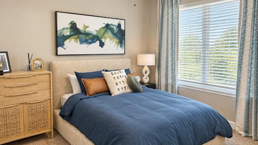 A bedroom with a bed, nightstand, and a painting on the wall.