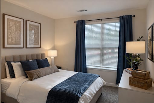 A bedroom with a large bed and a window with blue curtains.