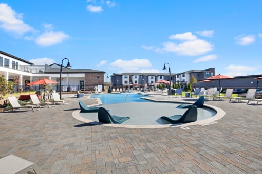 a large swimming pool with lounge chairs and umbrellas in front of a building