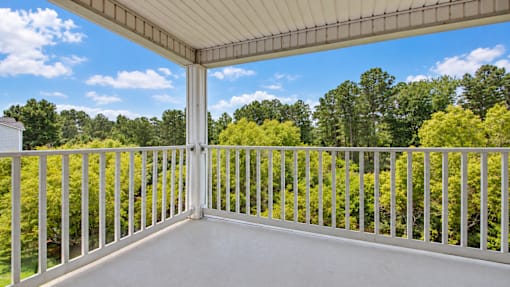 A white balcony with a metal railing overlooking a forest.