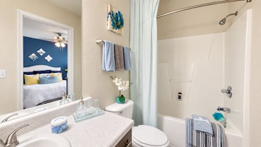 Bathroom with a vanity, white tub and shower combination, and a mirror reflecting the bedroom at Canterbury Apartments.