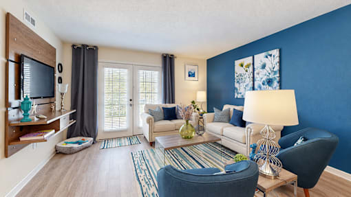 Furnished living room with a blue accent wall, cream seating and French doors at Canterbury Apartments in Myrtle Beach, SC.