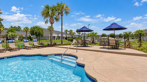 Swimming pool steps with a handrail, lounge chairs and shaded tables at Canterbury Apartments in Myrtle Beach, SC.