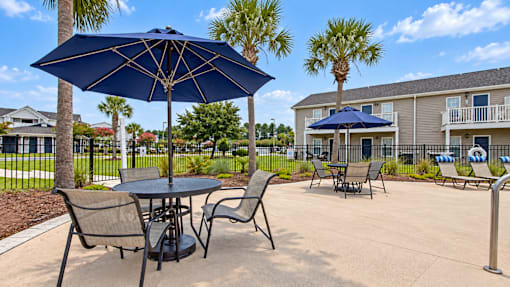 Poolside tables with navy umbrellas, lounge chairs and palm trees at Canterbury Apartments in Myrtle Beach, SC.