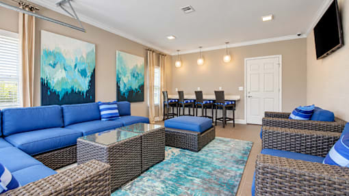 Resident lounge with blue sectional seating and a glass garage door overlooking the pool at Canterbury Apartments in Myrtle Beach, SC.