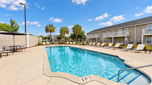 Outdoor swimming pool with entry steps, lounge chairs and palm trees at Canterbury Apartments in Myrtle Beach, SC.