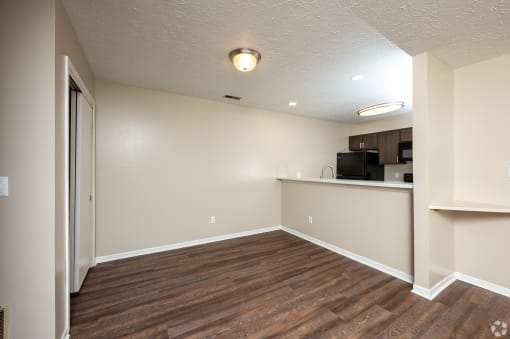 an empty living room with wood flooring and a kitchen