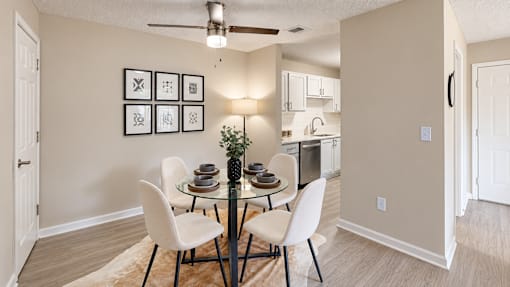 Dining area with a round glass table, four chairs, and a view into the kitchen at Icon Cartersville Apartments.
