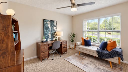 Furnished room with a desk, bookcase, and upholstered daybed beside a large window at Icon Cartersville.