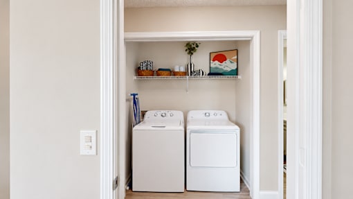 Laundry alcove with a white washer and dryer beneath a storage shelf at Icon Cartersville Apartments.