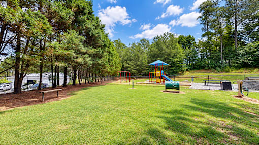 Open grassy area with trees, a playground, and dog agility features at Icon Cartersville Apartments.
