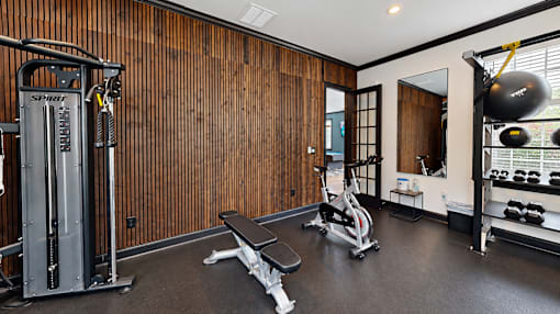 Fitness room with a cable machine, workout bench, exercise bike, and dumbbell rack at Icon Cartersville.