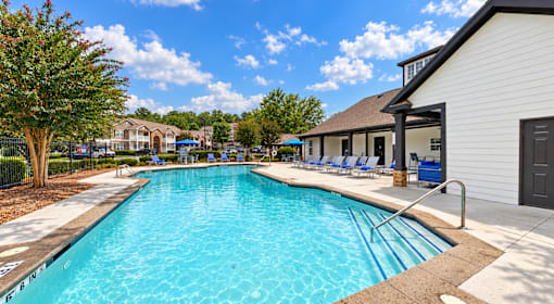Swimming pool with entry steps, lounge chairs, blue umbrellas, and clubhouse at Icon Cartersville Apartments.