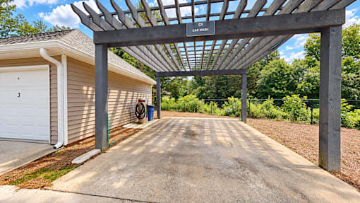 Covered car wash area beneath a wood pergola beside a garage at Icon Cartersville Apartments.