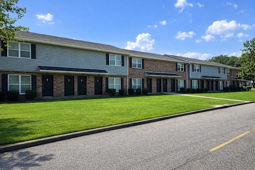 A row of houses with green lawns and trees in the background.