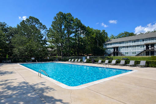A large swimming pool surrounded by trees and lounge chairs.