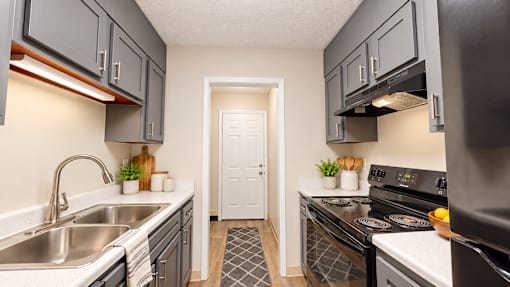 Galley kitchen with gray cabinets, black appliances, double sink, and white countertops at Madison Park Apartments & Townhomes.