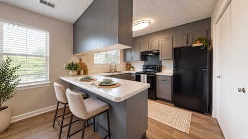 Apartment kitchen with gray cabinetry, breakfast peninsula, black appliances, and wood-style flooring at Madison Park in Birmingham, AL.