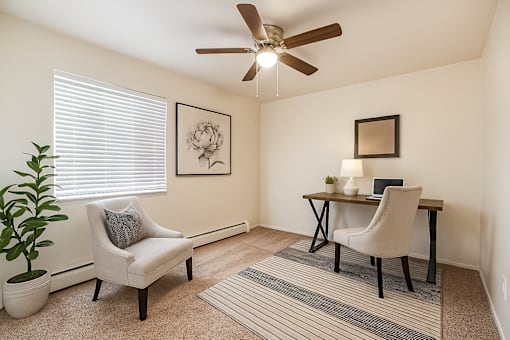 A room with a ceiling fan, a chair, a desk, and a potted plant.